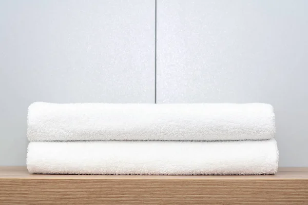 Dos toallas blancas cuidadosamente dobladas se encuentran en un estante de madera sobre un fondo de baldosas de cerámica . — Foto de Stock