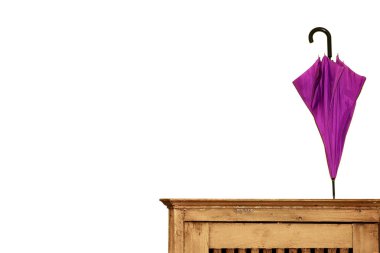 Mor renkli katlanmış bir şemsiye beyaz bir duvarın arka planına karşı ahşap bir göğüs üzerinde duruyor. Konsept iç, evde düzen, moda.