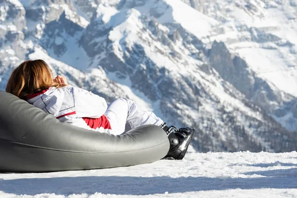 Une fille vêtue d'une veste blanche et de chaussures de ski se trouve sur un transat et regarde les montagnes . — Photo