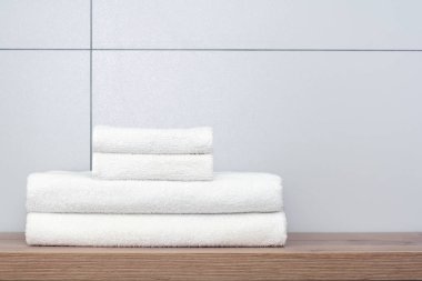 İki büyük ve iki küçük düzgünce katlanmış beyaz havlu seramik karoların arka planına karşı ahşap bir raf üzerinde yalan. 