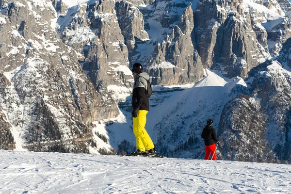 Een snowboarder in een zwarte jas en gele broek staat op een skipiste tegen de achtergrond van de berg. — Stockfoto