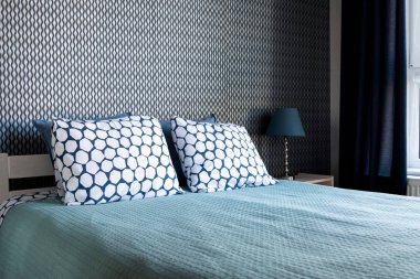 Bir çift kişilik yatak ile yatak odası karanlık bir duvara karşı bir lamba ve mavi bir perde ile bir komandite. Ev, tatil konsepti.