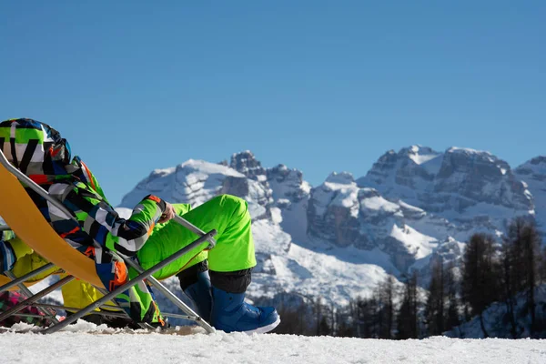 O cara o snowboarder senta-se em um salão de chaise e olha para as montanhas . — Fotografia de Stock