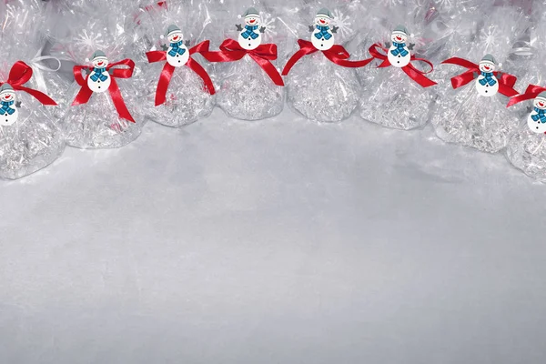 Prezenty świąteczne w postaci worków foliowych i przezroczystej folii wiązanej z kokardą z czerwonej wstążki na szczycie których są płatki śniegu na szarym tle. — Zdjęcie stockowe