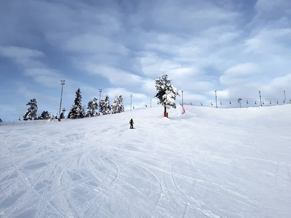 Ein Skifahrer rutscht vor dem Hintergrund eines wolkenverhangenen Himmels einen Berghang hinunter. — Stockfoto