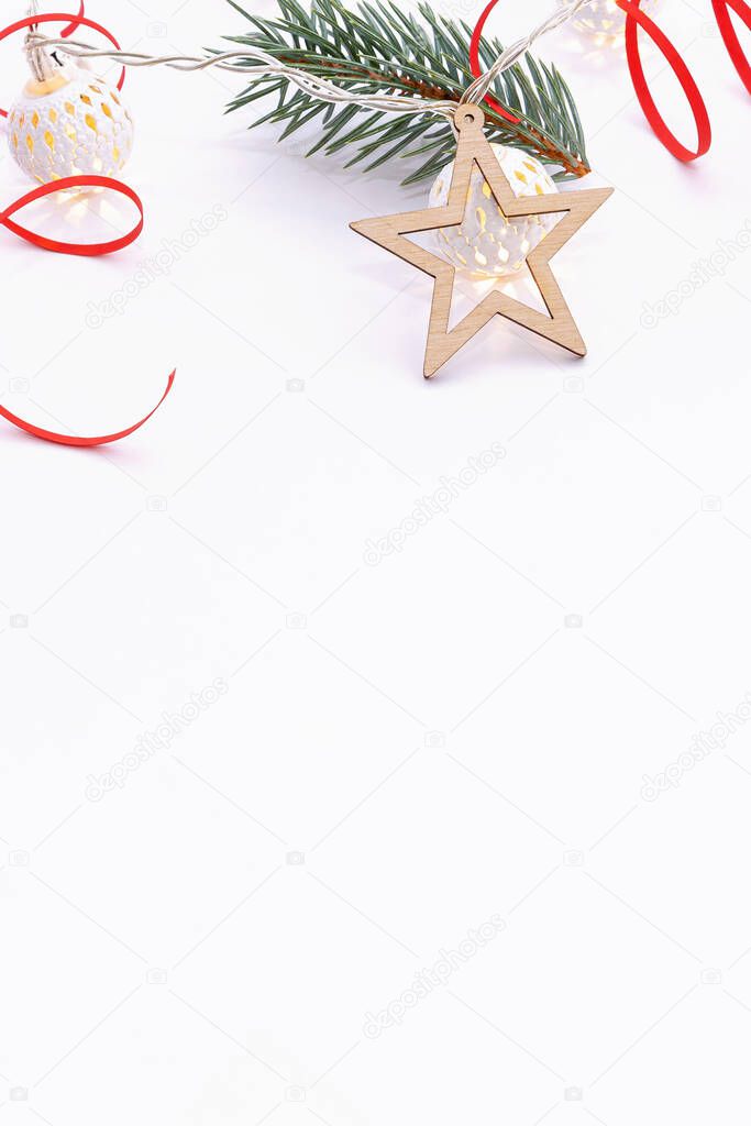 Christmas composition of fir branches, wooden stars, garlands of white luminous balls and red ribbon on a white background