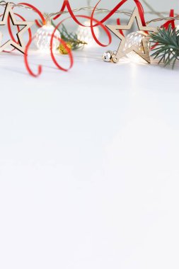 Noel kompozisyonu köknar dalları, tahta yıldızlar, beyaz toplardan oluşan çelenkler ve beyaz arka planda kırmızı kurdele..