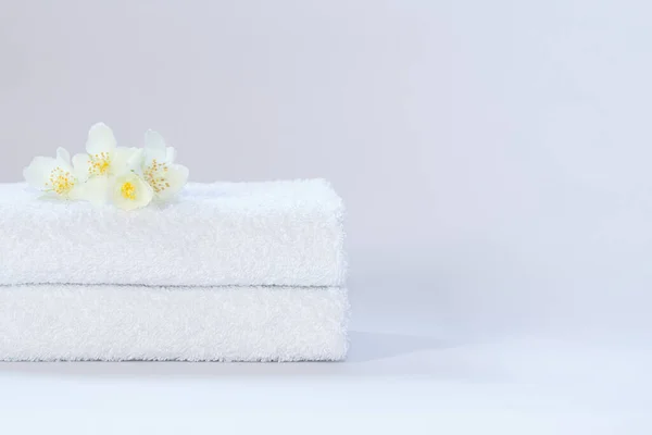 Dos toallas de felpa blancas cuidadosamente dobladas con una flor de jazmín sobre un fondo claro. — Foto de Stock