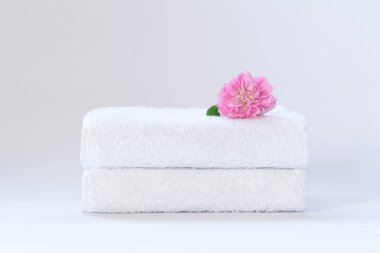İki beyaz katlanmış terry havlu ve açık arkaplanda bir gül çiçeği..