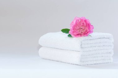 İki beyaz katlanmış terry havlu ve açık arkaplanda bir gül çiçeği..