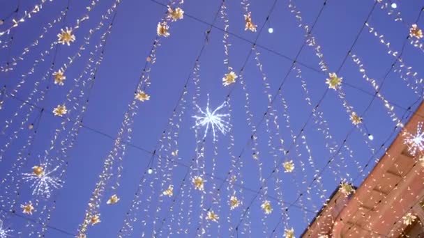 La calle está decorada con guirnaldas luminosas de luces que se balancean en el viento contra el telón de fondo del cielo azul y los edificios. Moscú. Calle Nikitskaya. — Vídeo de stock