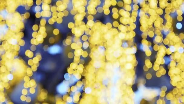 Bokeh de lumières jaunes et bleues d'une guirlande de Noël sur fond bleu qui balancent dans le vent. — Video