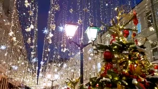 Uma árvore de Natal em Kuznetsky Most Street em Moscou contra o pano de fundo de guirlandas cintilantes e lâmpadas de rua. — Vídeo de Stock