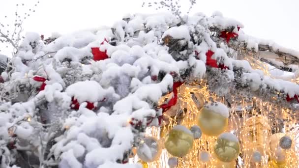 Décorations de Noël recouvertes de neige sur les toits des maisons dans les rues de Moscou et guirlandes lumineuses se développant dans le vent. — Video