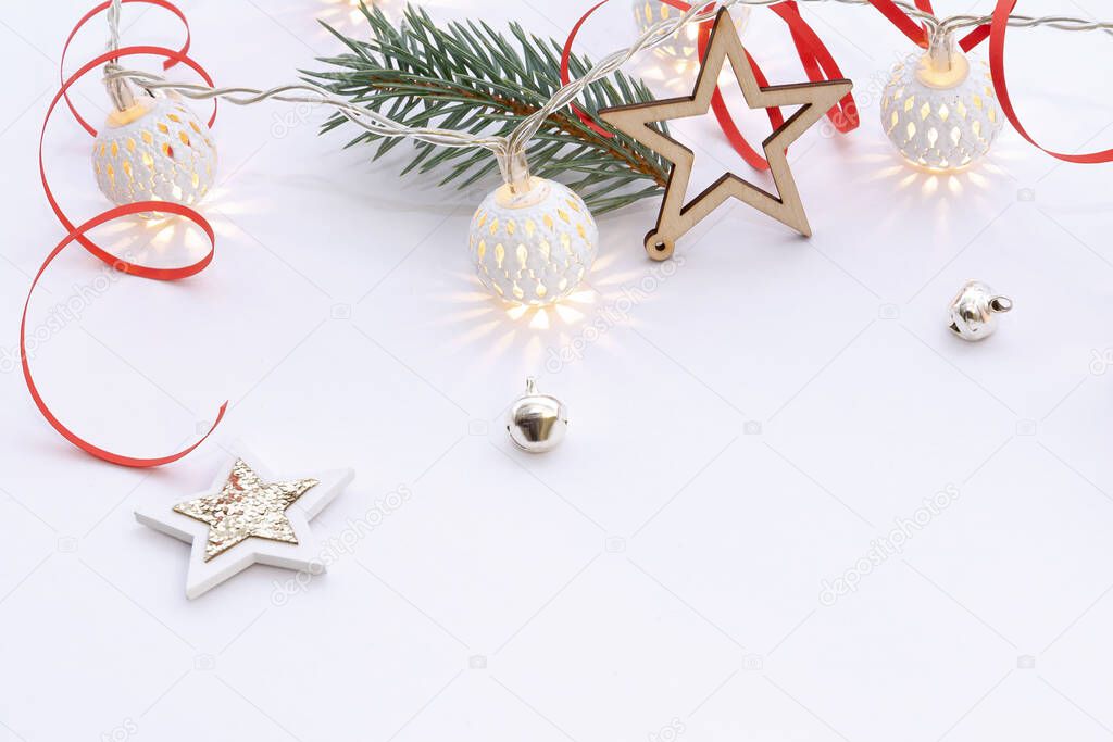 Christmas composition of wooden stars with sparkles, garlands of white luminous balls, fir branches and red ribbons on a white background