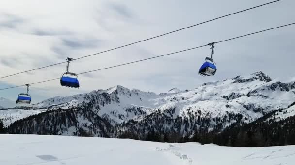 Utsikt över linbanan med blå stolsstugor rör sig utan människor mot bakgrund av snötäckta bergstoppar. Sport koncept, landskap. — Stockvideo