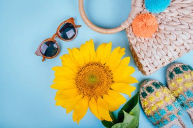 Güneş gözlüğü, espaddrille sandalet, hasır çanta ve mavi arka plan üzerinde parlak büyük sarı ayçiçeği ile moda flatlay. Flatlay tarzı.