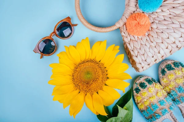 Güneş gözlüğü, espaddrille sandalet, hasır çanta ve mavi arka plan üzerinde parlak büyük sarı ayçiçeği ile moda flatlay. Flatlay tarzı.