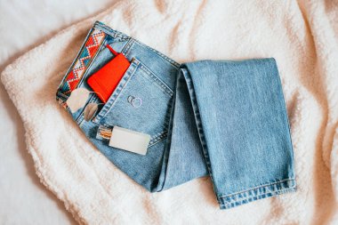 Mavi jeans, kırmızı defter, parfüm şişesi ve aksesuarları ile rahat moda flatlay. Yatakta minimalist flatlay.
