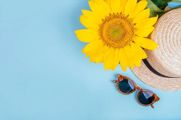 Güneş gözlüğü, saman hasır şapka şapka ile mavi arka plan üzerinde parlak büyük sarı ayçiçeği moda flatlay. Flatlay tarzı.