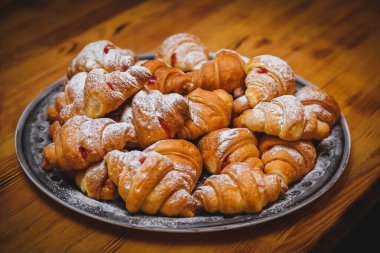 Büyük tabak ve bir sürü taze pişmiş kruvasan. Kruvasanın üstüne pudra şekeri. Lokanta, stand-up yemeği ya da ziyafet için fotoğraf. Partideki lezzetli yemekler.