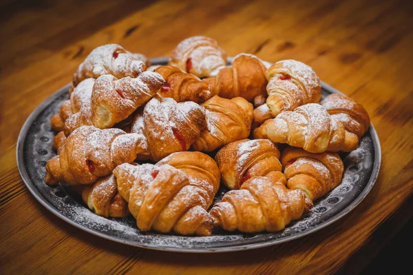 Büyük tabak ve bir sürü taze pişmiş kruvasan. Kruvasanın üstüne pudra şekeri. Lokanta, stand-up yemeği ya da ziyafet için fotoğraf. Partideki lezzetli yemekler.