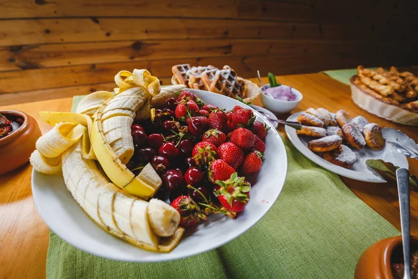 Bir sürü lezzetli muzlu çilek ve çilekli büyük tabak. Lokanta, stand-up yemeği ya da ziyafet için fotoğraf. Partideki sağlıklı ve lezzetli yemekler. Et lokantasında yaz kahvaltısı