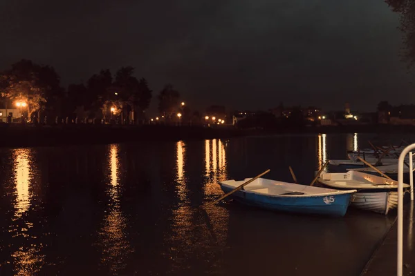 night promenade small boats moored to the shore. lights reflected from the water on the promenade with boats. white-blue boats and gold reflection on the river at night