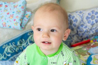 Bir yıl eski bebek oturma ve dikkatle bir yer arıyorum. Koyun ile ışık Yeşil elbiseli küçük neşeli çocuk.