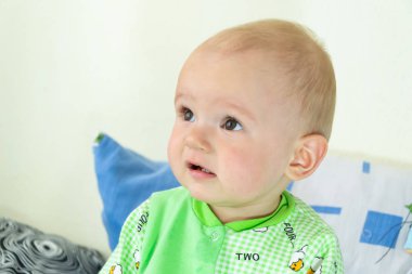 Bir yıl eski bebek oturma ve dikkatle bir yer arıyorum. Koyun ile ışık Yeşil elbiseli küçük neşeli çocuk.