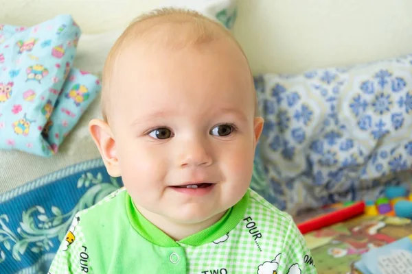 Bir yıl eski bebek oturma ve dikkatle bir yer arıyorum. Koyun ile ışık Yeşil elbiseli küçük neşeli çocuk.