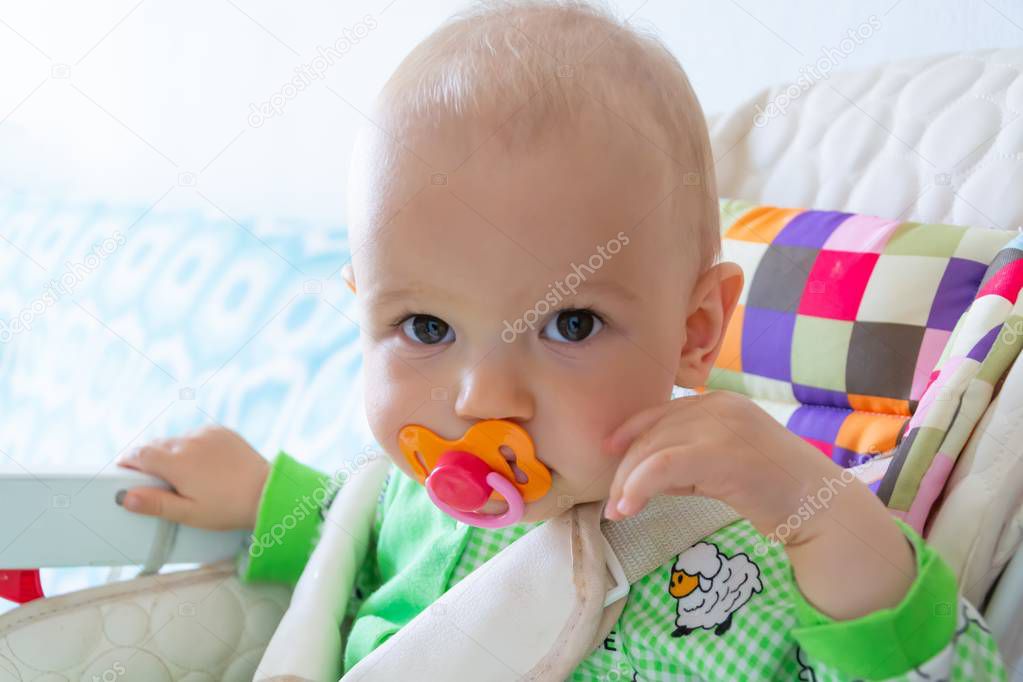 One year old baby nibbles / sucks on a rubber nipple because his teeth are being cut. Little cheerful boy in a light green suit with sheep.