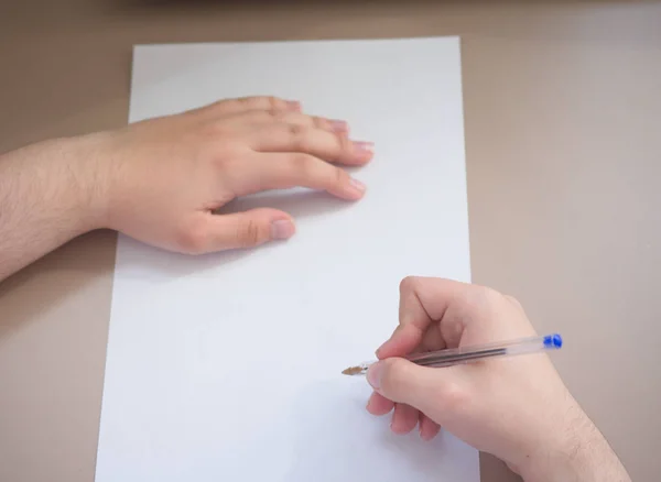 Człowiek pisania na dole kawałek papieru z długopisem, a on trzyma papier lewą ręką — Zdjęcie stockowe