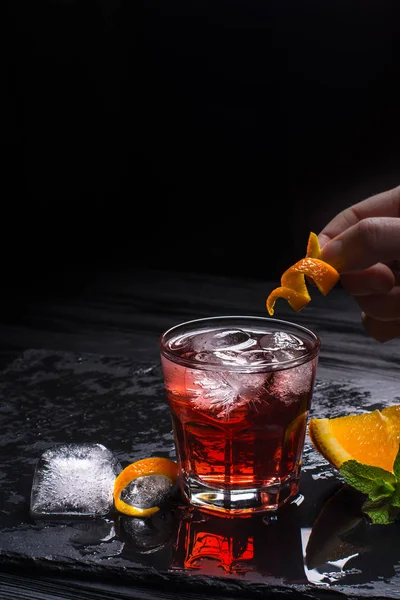 Mezcal Negroni cocktail göra. Italiensk aperitivo. Hand sätter apelsinskal i en cocktail. — Stockfoto