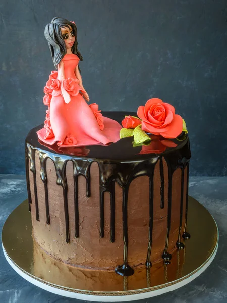 Handmade cake covered a black chocolate glaze with figure of a girl in a red dress and a red rose on a dark background