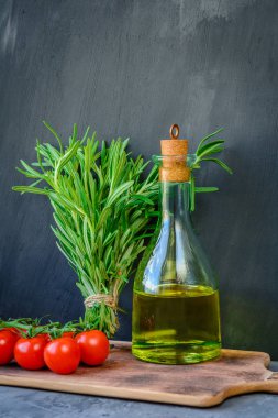 Taze biberiye demet, domates ile bir şişe biberiye yağı veya zeytinyağı üzerinde kesme taş arka plan üzerinde kurulu.