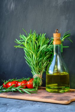 Taze biberiye demet, domates ile bir şişe biberiye yağı veya zeytinyağı üzerinde kesme taş arka plan üzerinde kurulu.