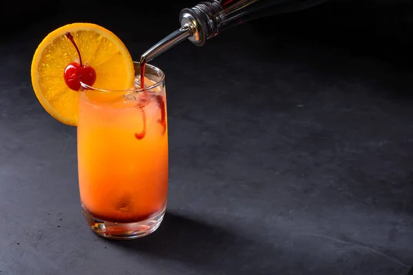 カクテルのテキーラ サンライズを作る グレナディンは ゆっくりと氷 テキーラとオレンジ ジュースをグラスに注いだ コピー スペースと石の背景 — ストック写真