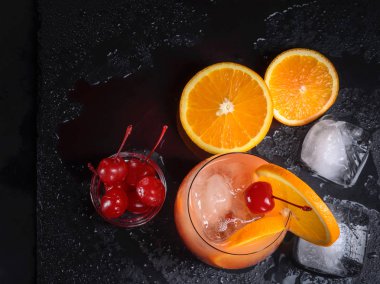 Tekila Sunrise kokteyli, portakal, buz küpleri ve ıslak bir siyah arduvaz tepsi maraschino kirazı.