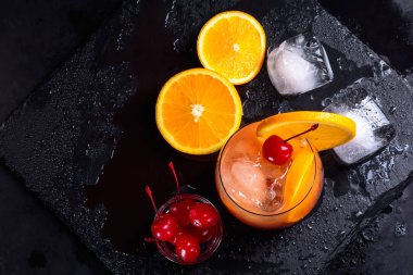 Tekila Sunrise kokteyli, portakal, buz küpleri ve ıslak bir siyah arduvaz tepsi maraschino kirazı. Düz kopya alanı ile yatıyordu.