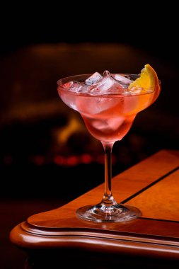 Arka planda yanan şömine ile klasik eski moda ahşap masa üzerinde turuncu dilim ile Negroni kokteyl