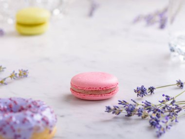 Görüntünün ortasında bir pembe makarna ve sprigs lavanta, önünde bir leylak donut, arkasında bir makarna, beyaz mermer masa