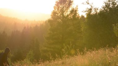 Gün batımında sırt çantası olan bir adam dağa çıkar. Adamların arkasında gün batımında arka ışıkta bir dağ ormanı var..
