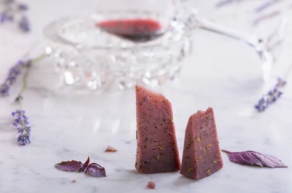 Два куска базальтового лавандового сыра, цветы лаванды и бокал красного вина на столешнице из белого мрамора — стоковое фото