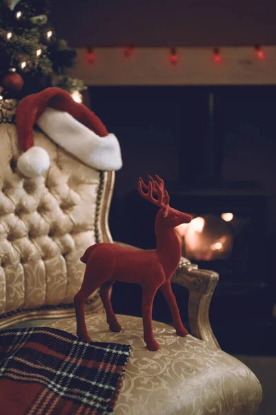 驯鹿和圣诞老人的帽子在椅子上由咆哮的原木火在圣诞节 — 图库照片