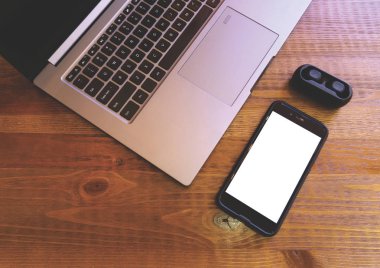 Ahşap arka planda dizüstü boş mobil ve kulaklıklar. Boş akıllı telefon ekranı ve TWS kulaklık ile mock up. Modern kablosuz kulaklıklar ve dizüstü bilgisayar.