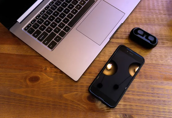 Portátil en blanco móvil y auriculares sobre fondo de madera. Finge con pantalla de teléfono inteligente en blanco y auriculares tws. Auriculares inalámbricos modernos y portátil . — Foto de Stock