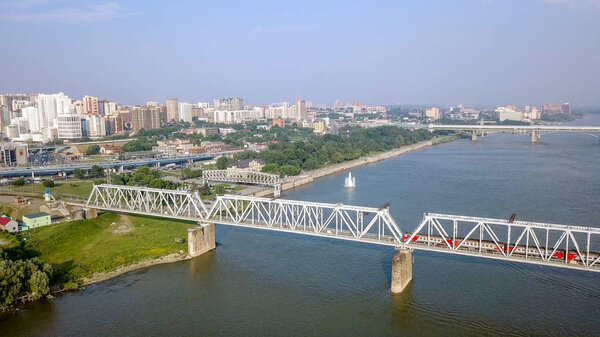 Электропоезд пересекает Обь. Первый железнодорожный мост в Новосибирске. Панорама города Новосибирска. Россия, Дрон
  