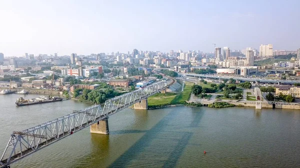 The electric train crosses the Ob river. First Railway Bridge in Novosibirsk. Panorama of the city of Novosibirsk. Russia, From Dron