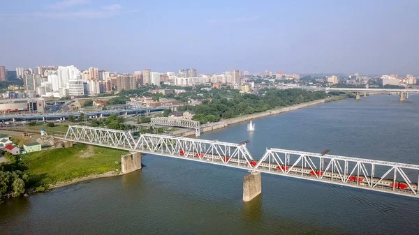 The electric train crosses the Ob river. First Railway Bridge in Novosibirsk. Panorama of the city of Novosibirsk. Russia, From Dron